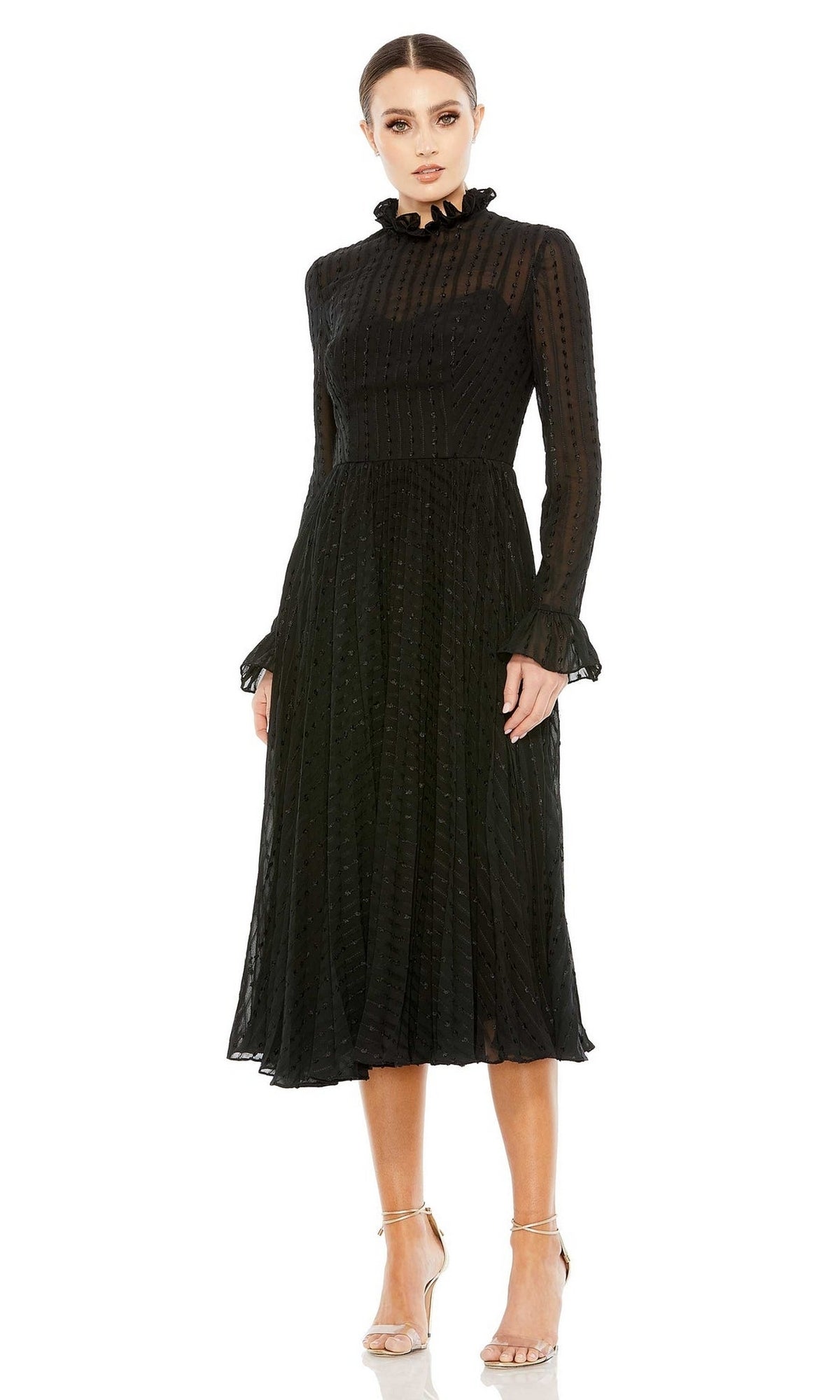 A woman wears the Short Wedding Guest Dress 49627 by Mac Duggal, a black long sleeve dress with a ruffled high neck, pleated knee-length skirt, and sheer polka-dot fabric, paired with strappy high-heeled sandals.